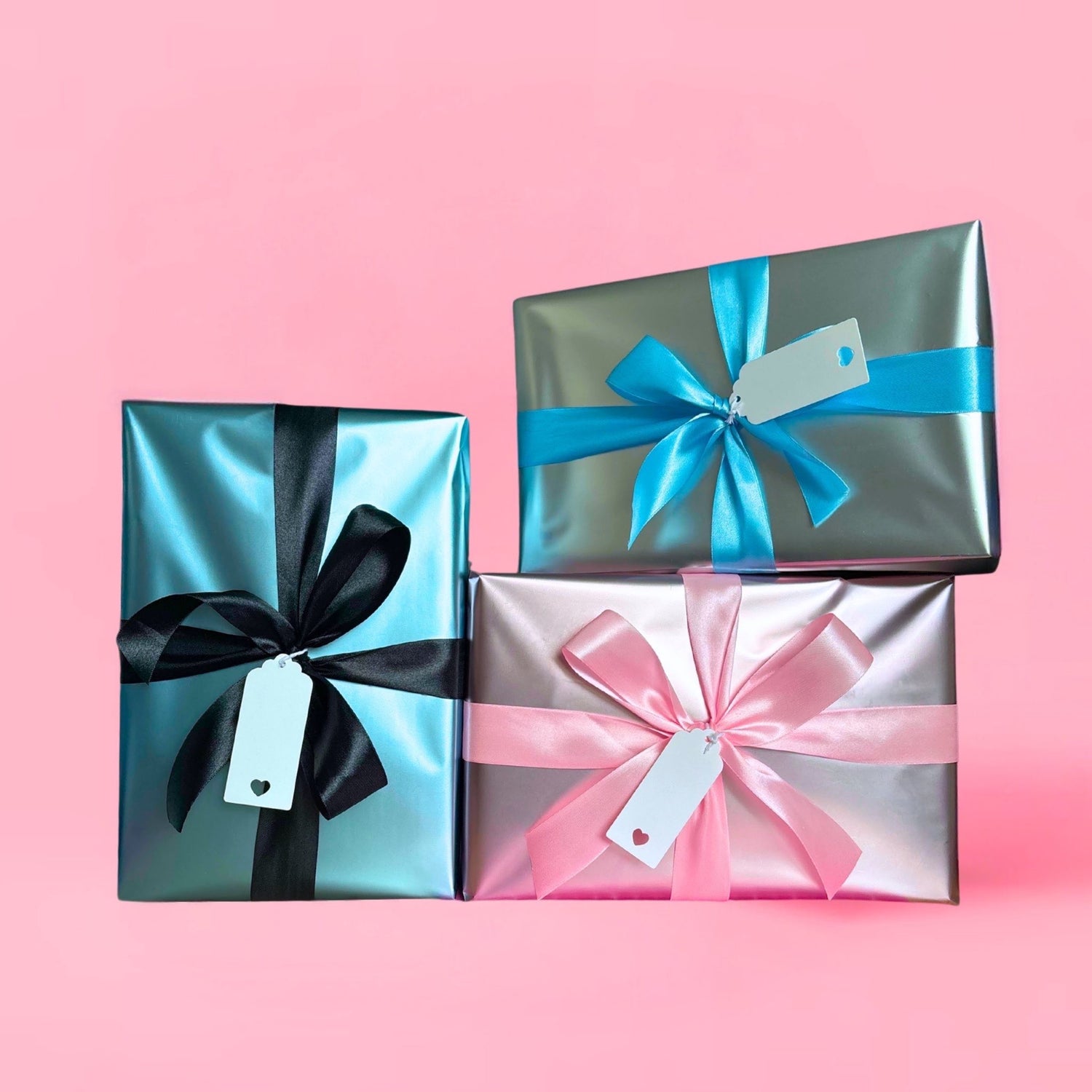 Three gift boxes wrapped in satin paper, with a satin ribbon bow tied around each one, and a gift tag attached.